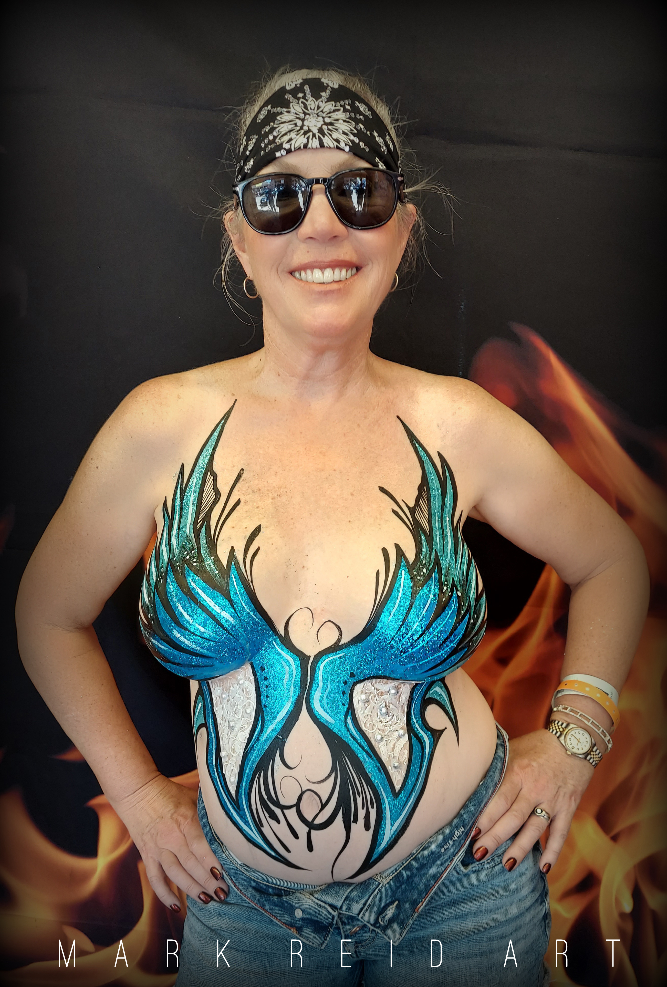 Woman wearing a black and white headband with a painted on top that looks similar to wings that a blue reaching from around her navel flowing up and over her breasts to her collar bone 