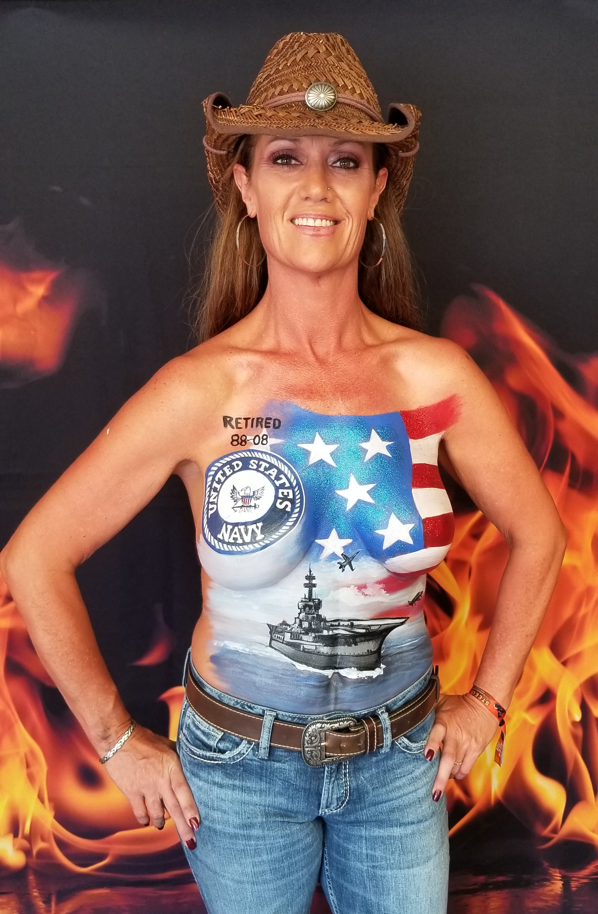 long haired brunette with a painting on her top half saluting the navy including naval ship painted on her abdomen and a flag above