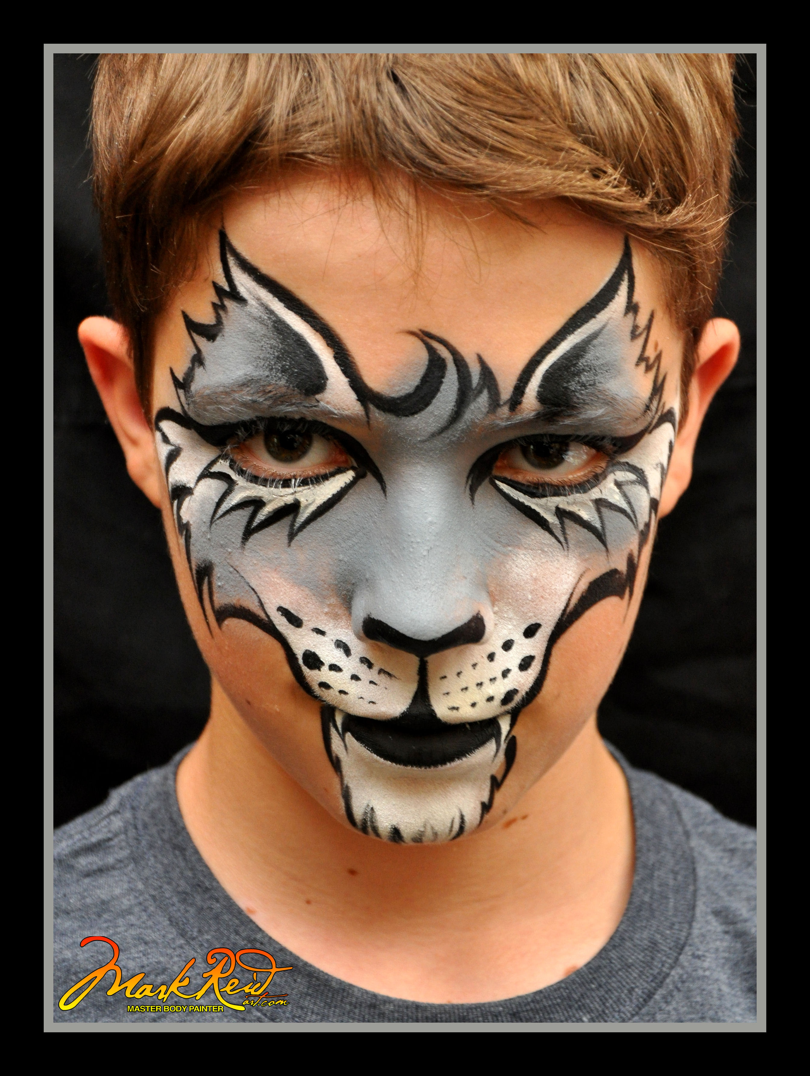 Young boy with a face painting of a mask on his face that looks like a cat on his nose and mouth with stylized lashes around his eyes