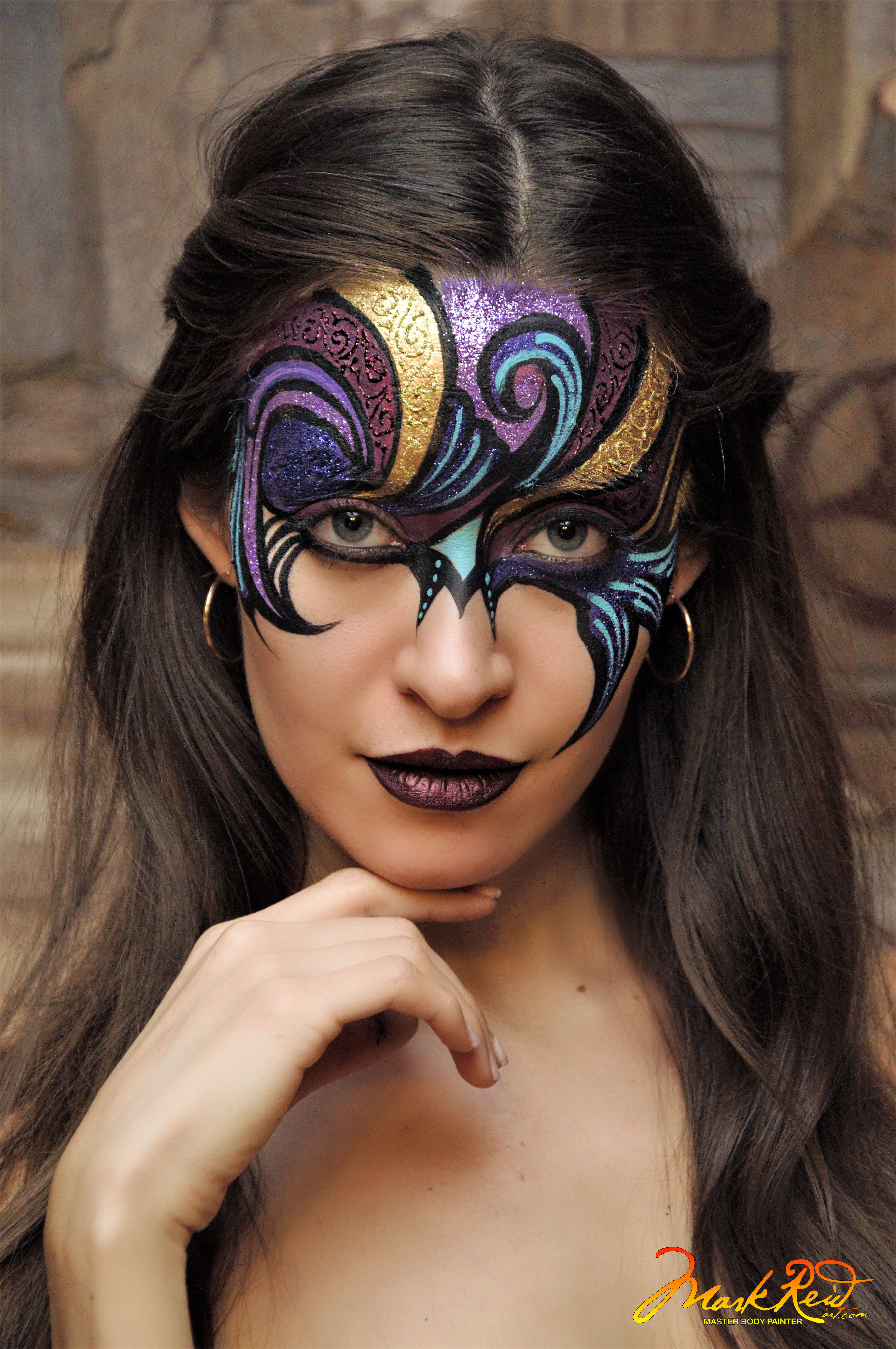 Brunette with long flowing hair and a painted on mask around her eyes and on her forehead. Very detailed mask in gold and purple mostly with lots of swirling lines