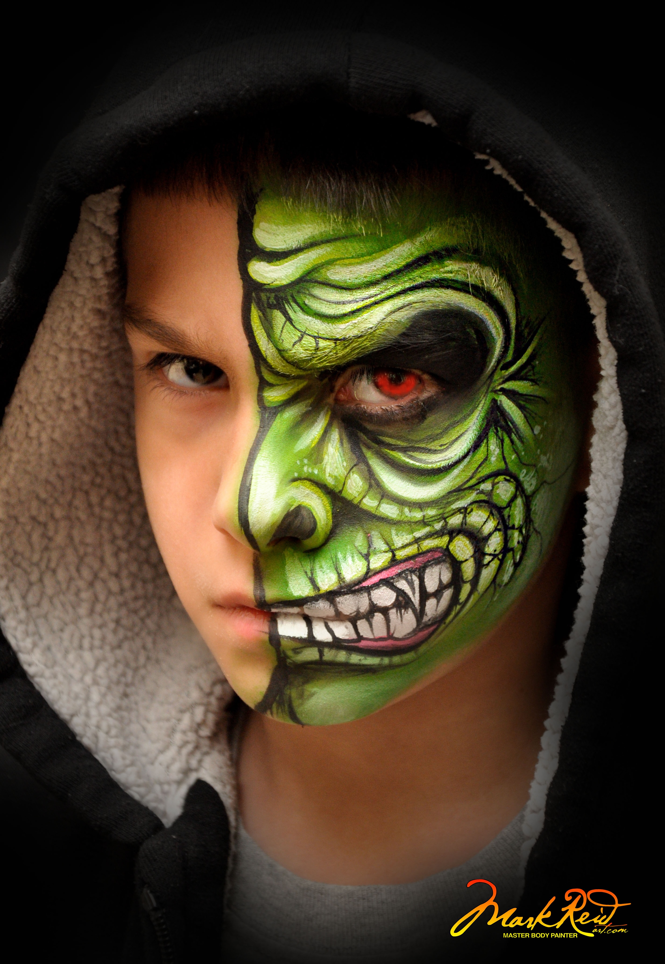 boy face painted with one half of his face not painted and the other half in a green moster with red eye