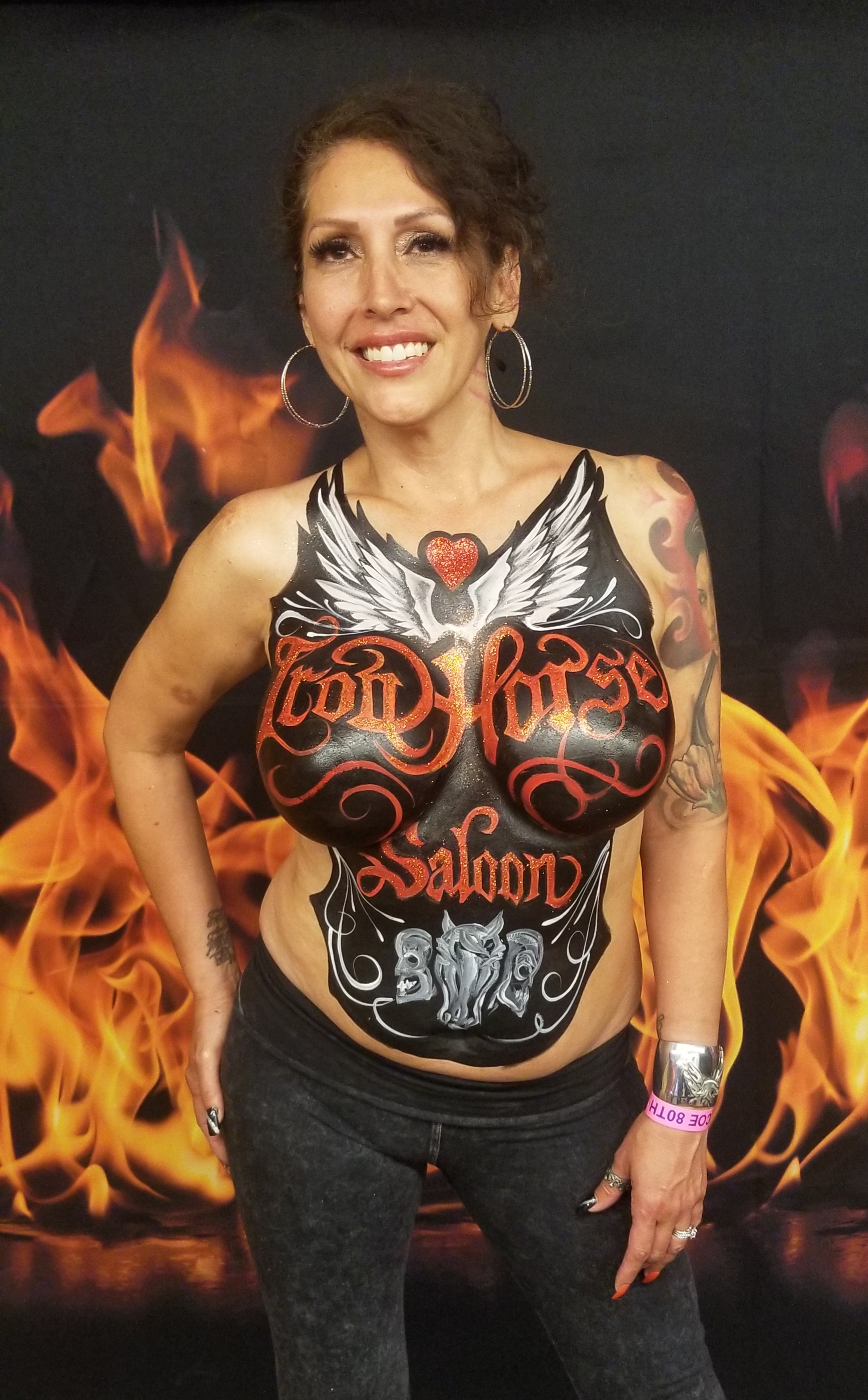 smiling brunette with a very detailed stylized Iron Horse Saloon body painting on her top half featuring wings and a heart
