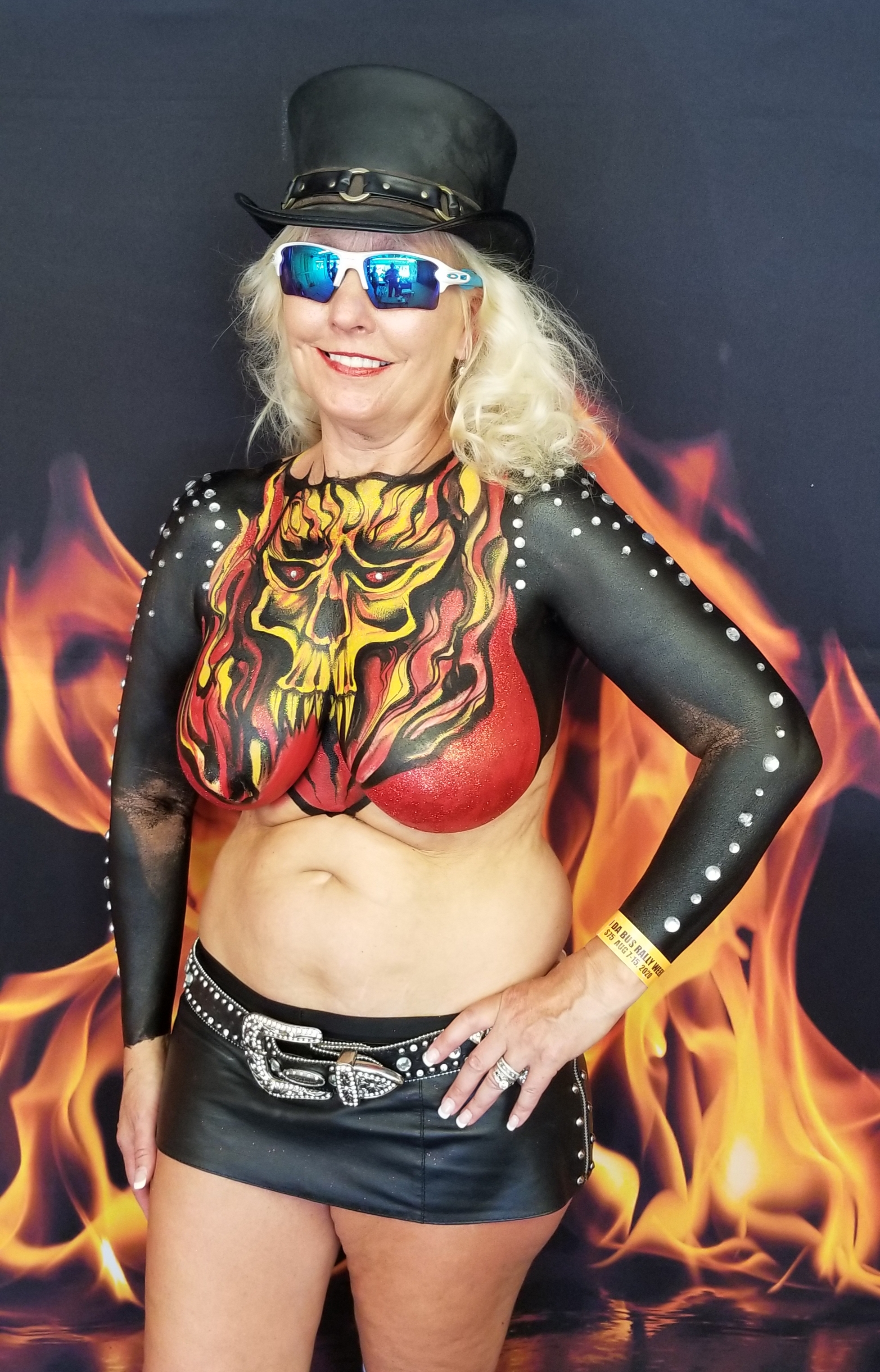 long haired blond in a leather top hat with a stylized red and orange skull on a black background painted on her top half